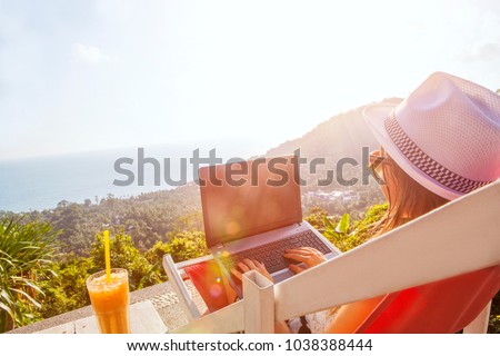 Girl freelance work typing on laptop and looking at monitor screen desktop with beautiful view background and cocktail outdoors sun sky and greens. Traveling with a computer concept. Place for text