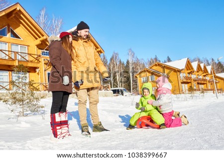 Young parents walking with their little kids on sled on bright winter afternoon out of town, low angle view