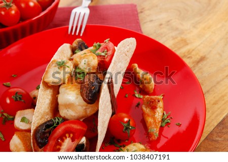 big mexican taco with tomatoes and mushroom, served with soup, fresh vegetables , on red crockery plates over wooden table with cutlery and napkin