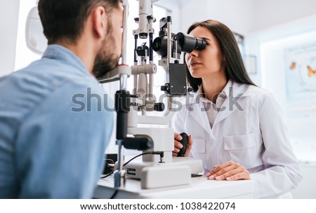 Attractive female doctor  ophthalmologist is checking the eye vision of handsome young man in modern clinic. Doctor and patient in ophthalmology clinic. Royalty-Free Stock Photo #1038422074