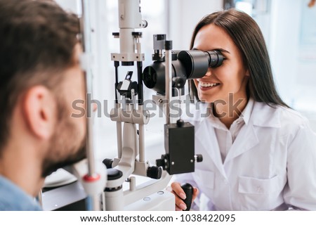 Attractive female doctor  ophthalmologist is checking the eye vision of handsome young man in modern clinic. Doctor and patient in ophthalmology clinic. Royalty-Free Stock Photo #1038422095