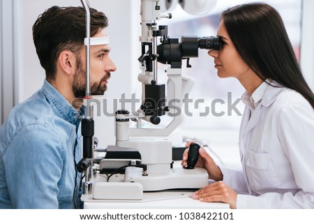 Attractive female doctor  ophthalmologist is checking the eye vision of handsome young man in modern clinic. Doctor and patient in ophthalmology clinic. Royalty-Free Stock Photo #1038422101