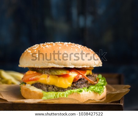 Delicious fresh tasty burger with beef, tomato, cheese and lettuce served and french fries on a wooden cutting board on dark background.
Street fast food
