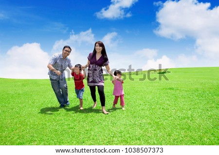 Picture of happy family playing together while running in the meadow with beautiful sky background