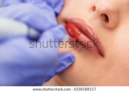 Young woman having permanent makeup on lips in beautician salon. Close up Royalty-Free Stock Photo #1038588517