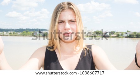 young blonde woman or blond teenager girl make selfie in front of river in city