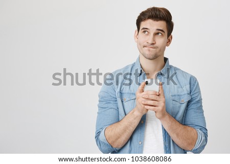 Portrait of handsome young adult with dreamy look, thinking while holding smartphone, isolated over white background. Son tries to made up message for his father, explaining why he took car Royalty-Free Stock Photo #1038608086