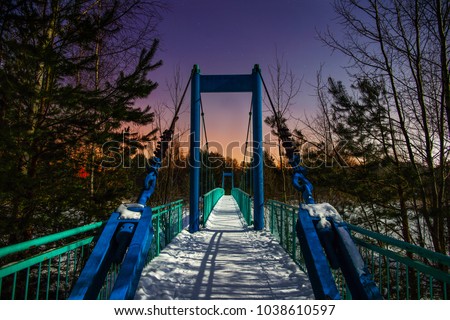 Winter night, starry sky. Snow-covered bridge across the frozen river in the moonlight