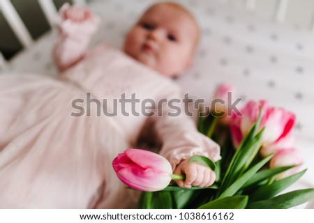 Close-up of newborn baby girl hand holding a bouquet of flowers pink tulips. New life, love and holiday concept. Women's Day. Mother's Day. Side view.