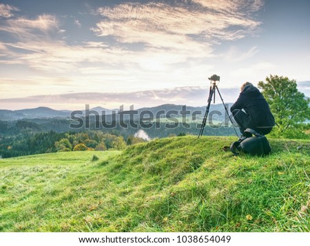 Long hair woman photographer stand on meadow and wait for sunrise. Short  grass and  misty and light fog above valley. Minute to sunrise