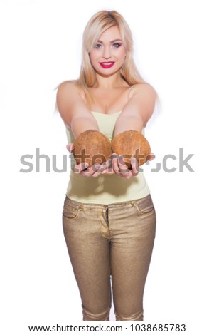 Studio portrait of a beautiful young blonde woman in a summer light yellow jersey and golden jeans. The girl is holding 2 coconuts. Concept - tropical fruits with a girl. Isolate