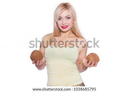 Studio portrait of a beautiful young blonde woman in a summer light yellow jersey and golden jeans. The girl is holding 2 coconuts. Concept - tropical fruits with a girl. Isolate