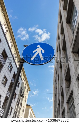 Blue and white circular road sign. Pedestrian zone. On the sides two vintage style buildings. Blue sky and white clouds. Bottom view.