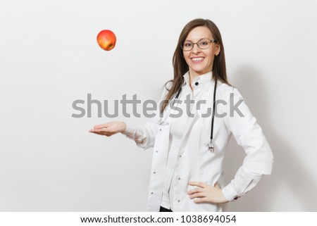 Smiling confident pretty young doctor woman with stethoscope, glasses isolated on white background. Female doctor in medical gown throwing up red apple. Healthcare personnel, health, medicine concept