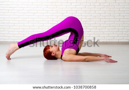 red-haired young girl in a bright sports suit engaged in yoga against a light brick wall