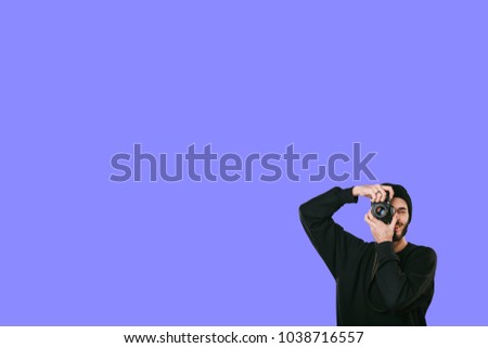 Stylish digital photographer with a beard in black shirt and casual hat. Isolated on blue background, white place for your descripition concept.