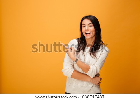 Portrait of a happy young woman pointing finger away at copy space isolated over yellow background