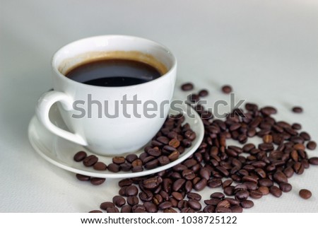 Black coffee in white glass and coffee beans placed on a white background.
