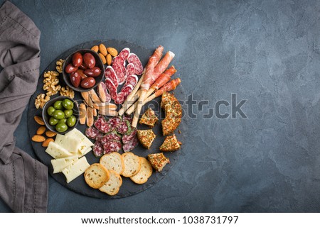 Still life, food and drink, holidays concept. Assortment of spanish tapas or italian antipasti with meat, ham, olives, cheese, nuts and bread on a black table. Top view flat lay copy space background