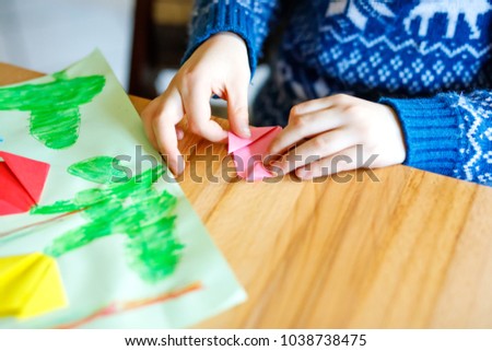 Closeup of hands of little kid making tulip flowers origami for a postcard for mother's day or birthday.