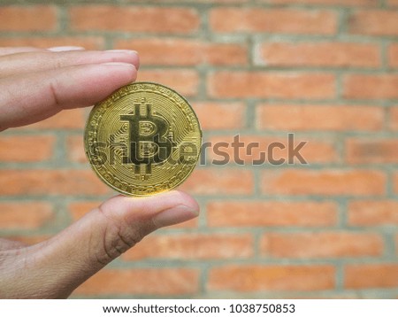Close-up of woman hand holding a bitcoin coin with brick wall background.