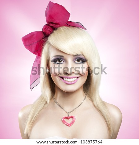 Beautiful young blond woman as doll with huge bow and plastic heart on pink background