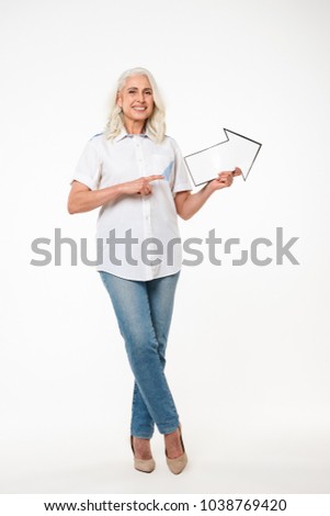 Full length portrait of a happy mature woman pointing away with an arrow isolated over white background