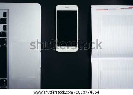 paper notebook and digital notebook with a smartphone in the middle on a black background