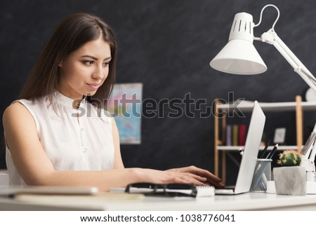 Young happy successful travel agent sitting at the table and working on laptop, copy space