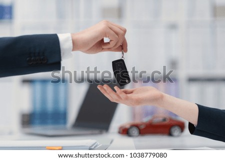 Woman purchasing a new car: she is signing a contract and receiving car keys from the agent