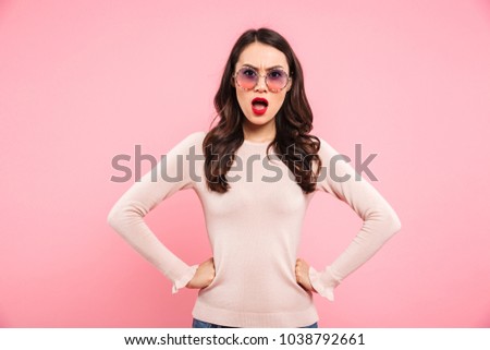 Photo of outraged angry woman in casual holding hands on waist and looking on camera in resentment isolated over pink background