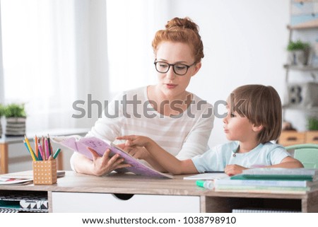 Young boy doing homework during extra-curricular classes with a tutor Royalty-Free Stock Photo #1038798910