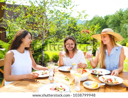Happy female friends with glasses of lemonade at dining table in lawn
