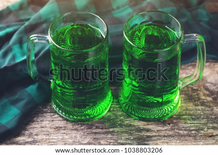 Two mug of green beer on the rustic wooden background.