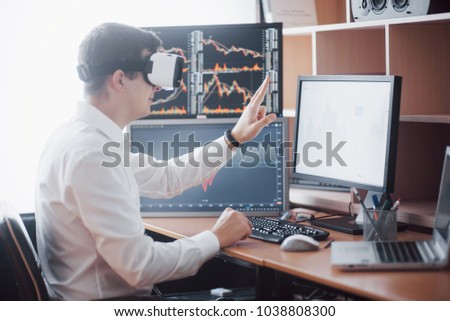 Businessman in virtual reality trading on stock market. Multiple computer screens ful of charts and data analyses in background.