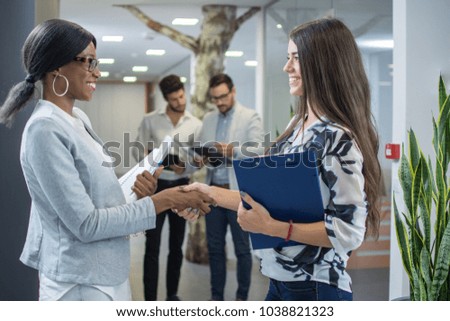 Two businesswomen shaking hands in modern office.