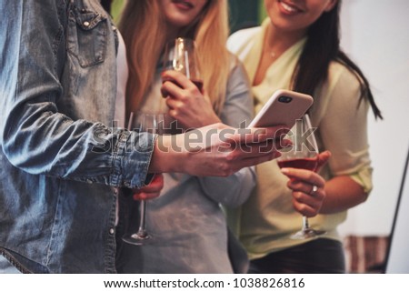 Picture presenting a happy group of girl friends with red wine. Together they see a photo on a smartphone.