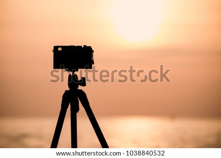 silhouette of vintage camera on tripod shooting beautiful calm sea with sun reflection on water at sunrise or sunset, image with copyspace