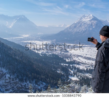 Man enjoys the view and looks down on Garmisch-Partenkirchen and Farchant and takes pictures with his smartphone