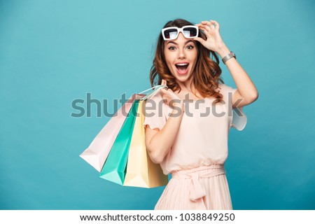 Portrait of an excited beautiful girl wearing dress and sunglasses holding shopping bags isolated over blue background Royalty-Free Stock Photo #1038849250