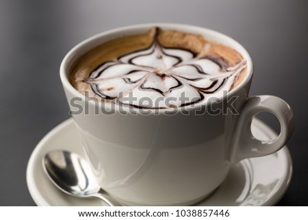 a closeup of a  cappuchino in a white cup with chocolate art on the top