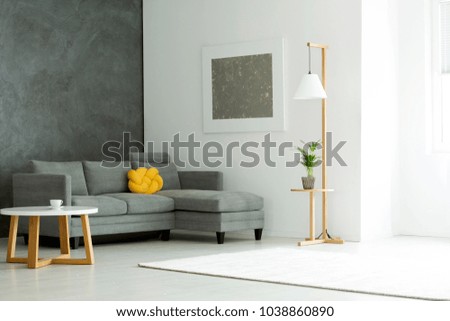 Grey painting on white wall above sofa with yellow pillow in apartment interior with plant and table