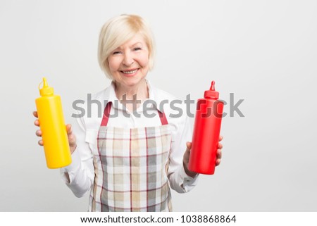 Great picture of old woman holding two bottles of sauses in her hands. She want to cook some tasty food for her beloved. Isolated on white background.