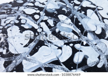 Ice texture of Lake Baikal with frozen white air bubbles in clear blue ice with cracks. Natural winter background