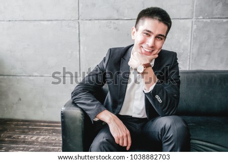 Young man businessman sitting on a black sofa holding hand to face