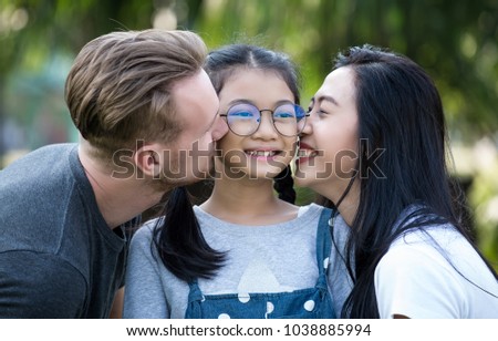 Portrait of beautiful young parents and their cute daughter hugging and kissing in public park,Happy parents kissing daughter,Family holiday vacation togetherness kiss love,Children and people concept