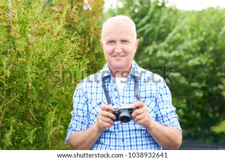 Portrait of smiling senior man taking pictures in park using vintage photo camera while travelling and looking at camera