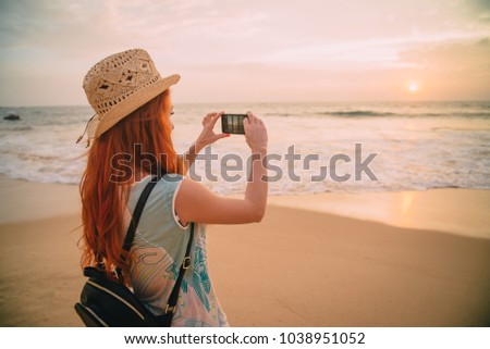 young woman tourist taking photo with smartphone on the beach at sunset