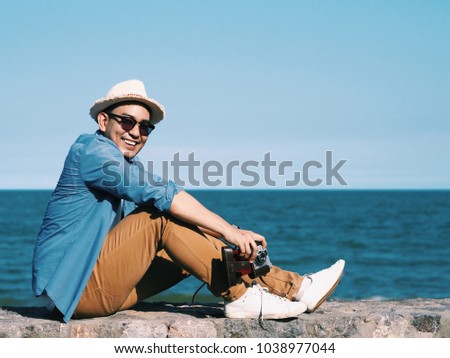 Asian travel man holding vintage camera,he standing over blue sky background.