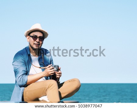 Asian travel man holding vintage camera,he standing over blue sky background.